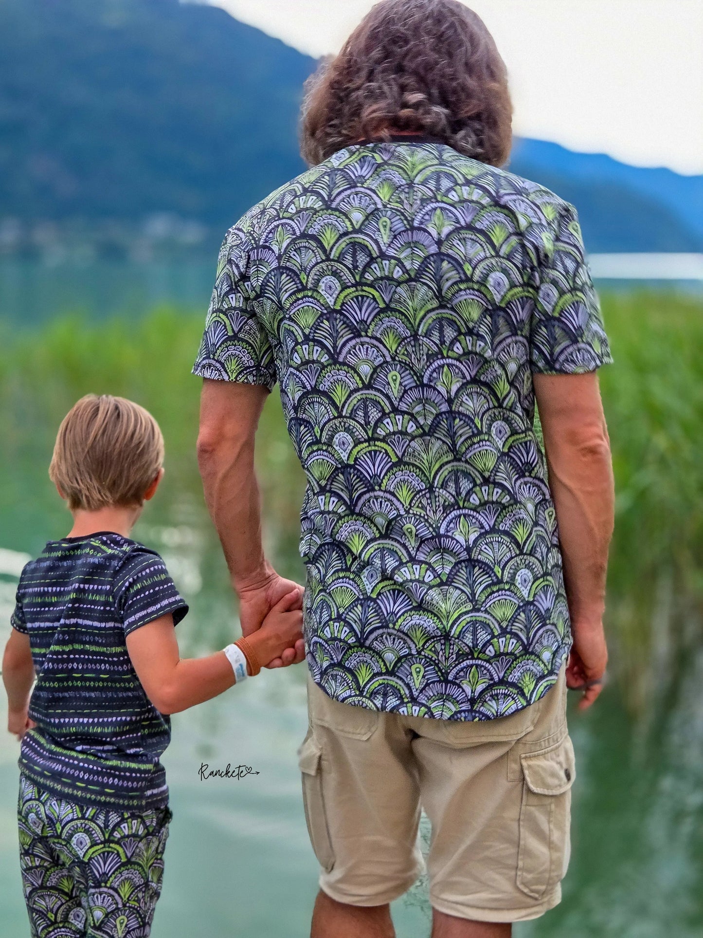 Vater und Sohn sitzen am See in selbstgenähten Outfits aus dem grün-schwarzen Ornamentstoff.