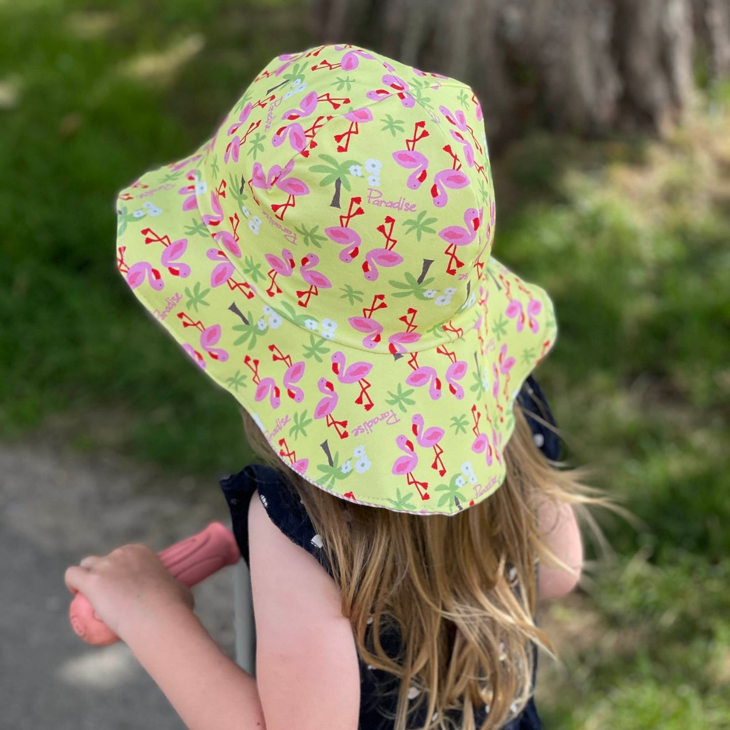 Schnittmuster Sommerhut Salva aus gelbem Jersey mit Flamingo-Print – Kind trägt selbstgenähten Sommerhut im Freien, breite Krempe, lebhaftes Sommermuster