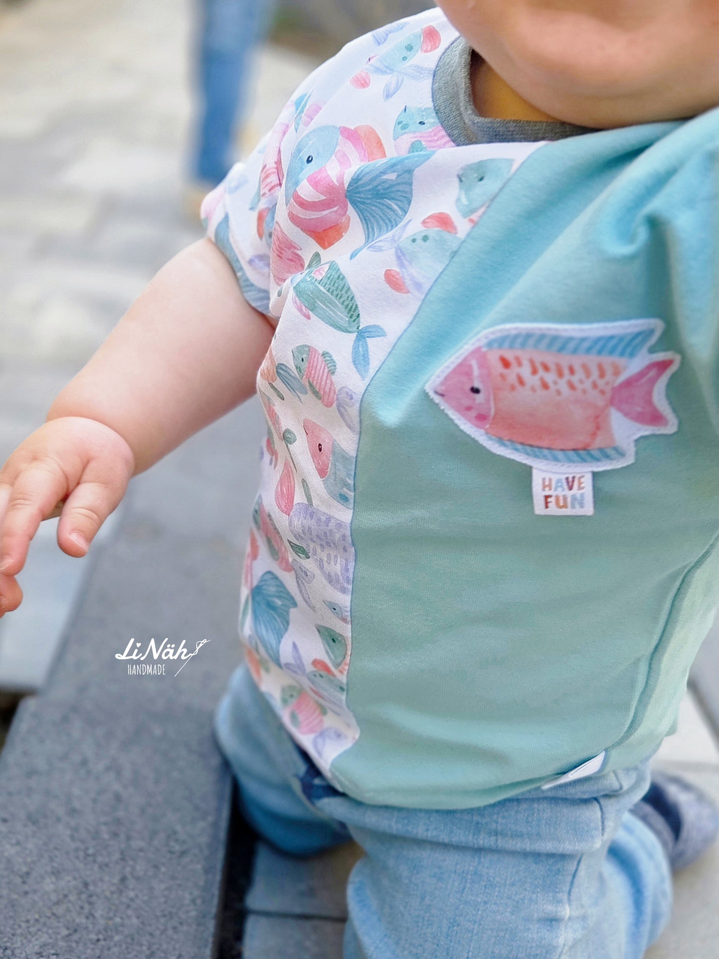Kinderstoff mit bunten Fischen Fishtales Weiß – selbst genähtes Babybody kombiniert mit mintfarbenem Uni-Jersey und aufgenähter Fisch-Applikation. Reaktivdruck Meterware, Öko-Tex Standard 100.