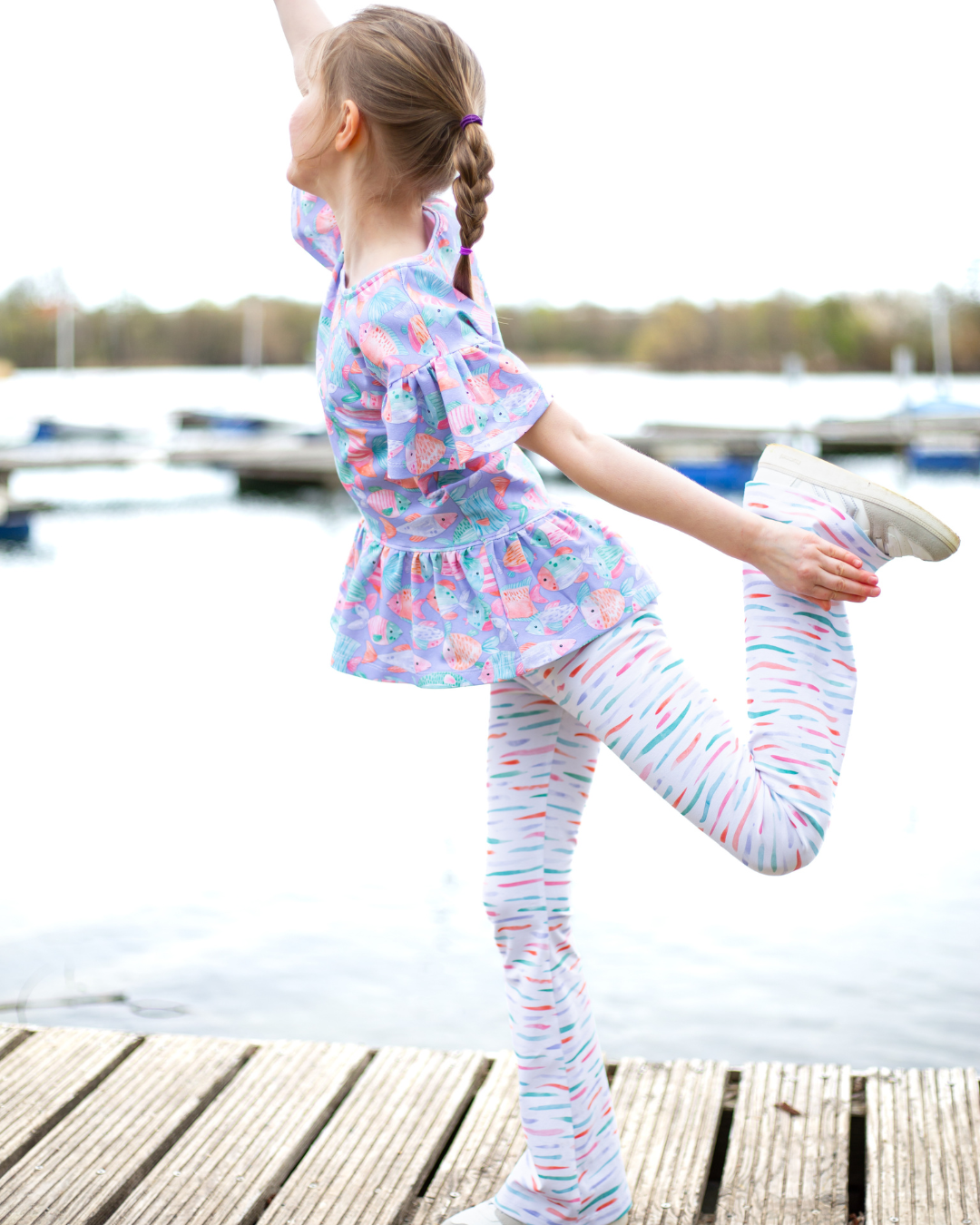 Kinderstoff mit Fischen nähen – Fishtales Lila als Peplum-Shirt mit Rüschenärmeln und Leggings aus weißem Kombistoff mit bunten Streifen. Digitaldruck auf Öko-Tex zertifizierten Stoffqualitäten.