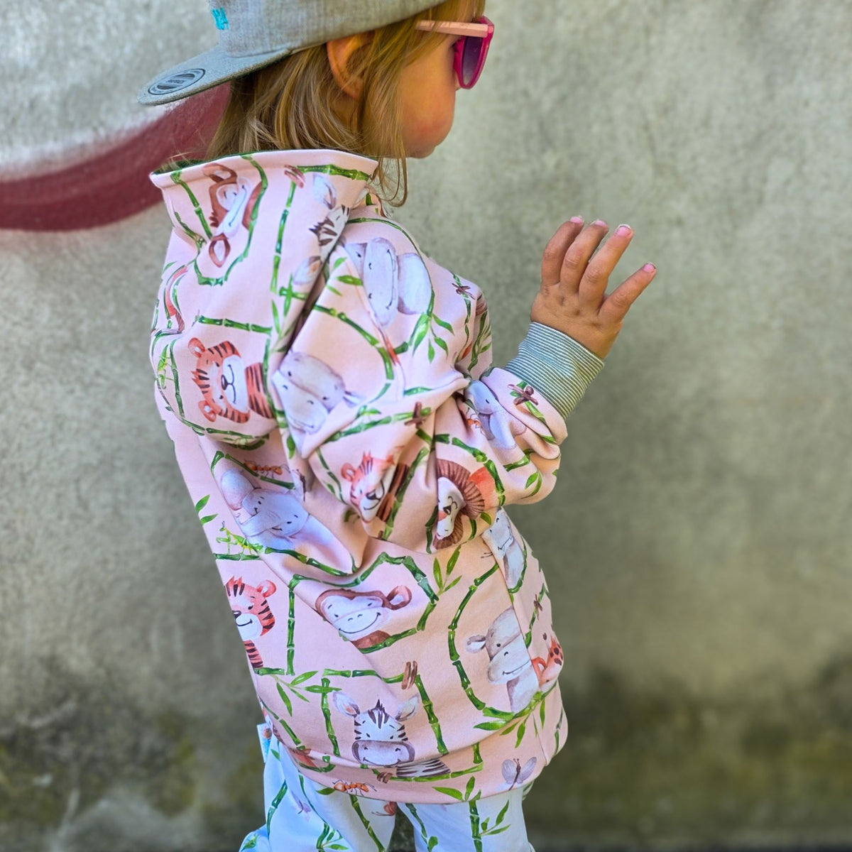 Kind von der Seite in einem Hoodie mit Kapuze aus Kinderstoff mit Safari-Tieren auf Pfirsich