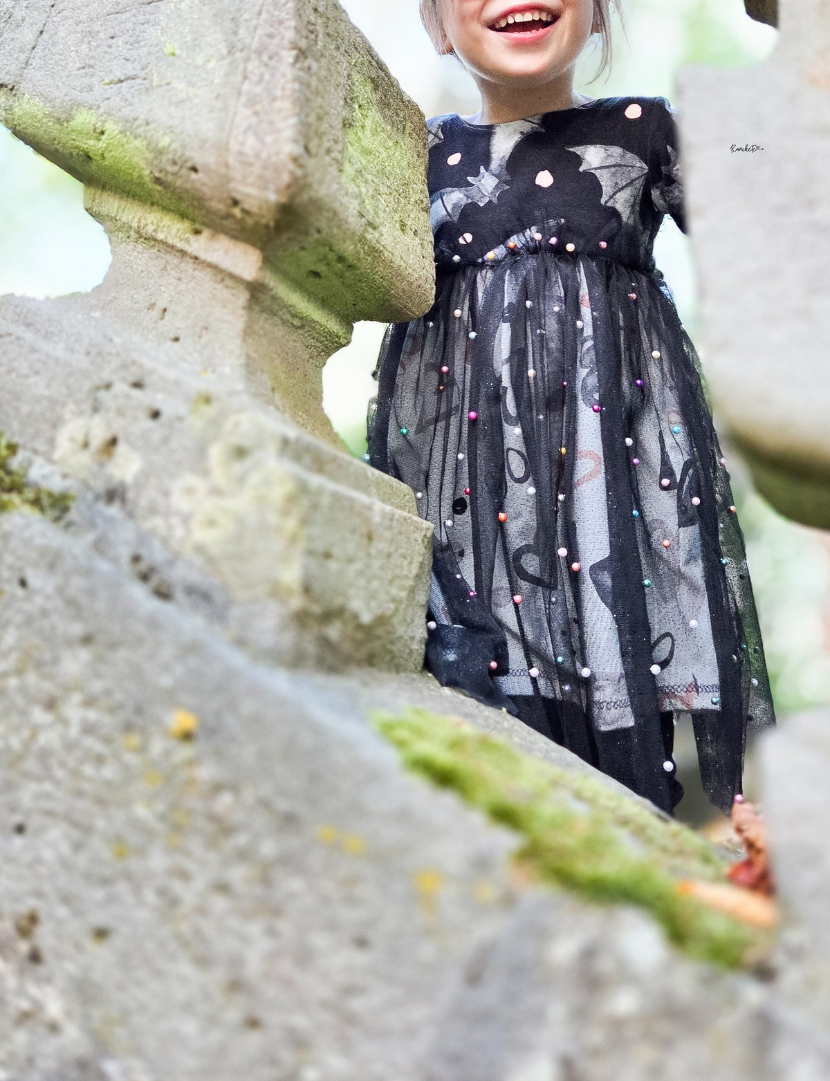 Lachendes Kind in einem Kleid aus Jersey mit grauen Fledermäusen auf Schwarz, genäht von Ranckete