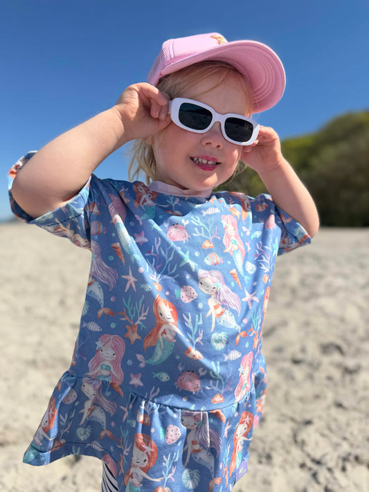 Kind am Strand im selbstgenähten T-Shirt aus Meerjungfrau Stoff in Blau mit handgemalten Meerjungfrauen, Seesternen und Muscheln