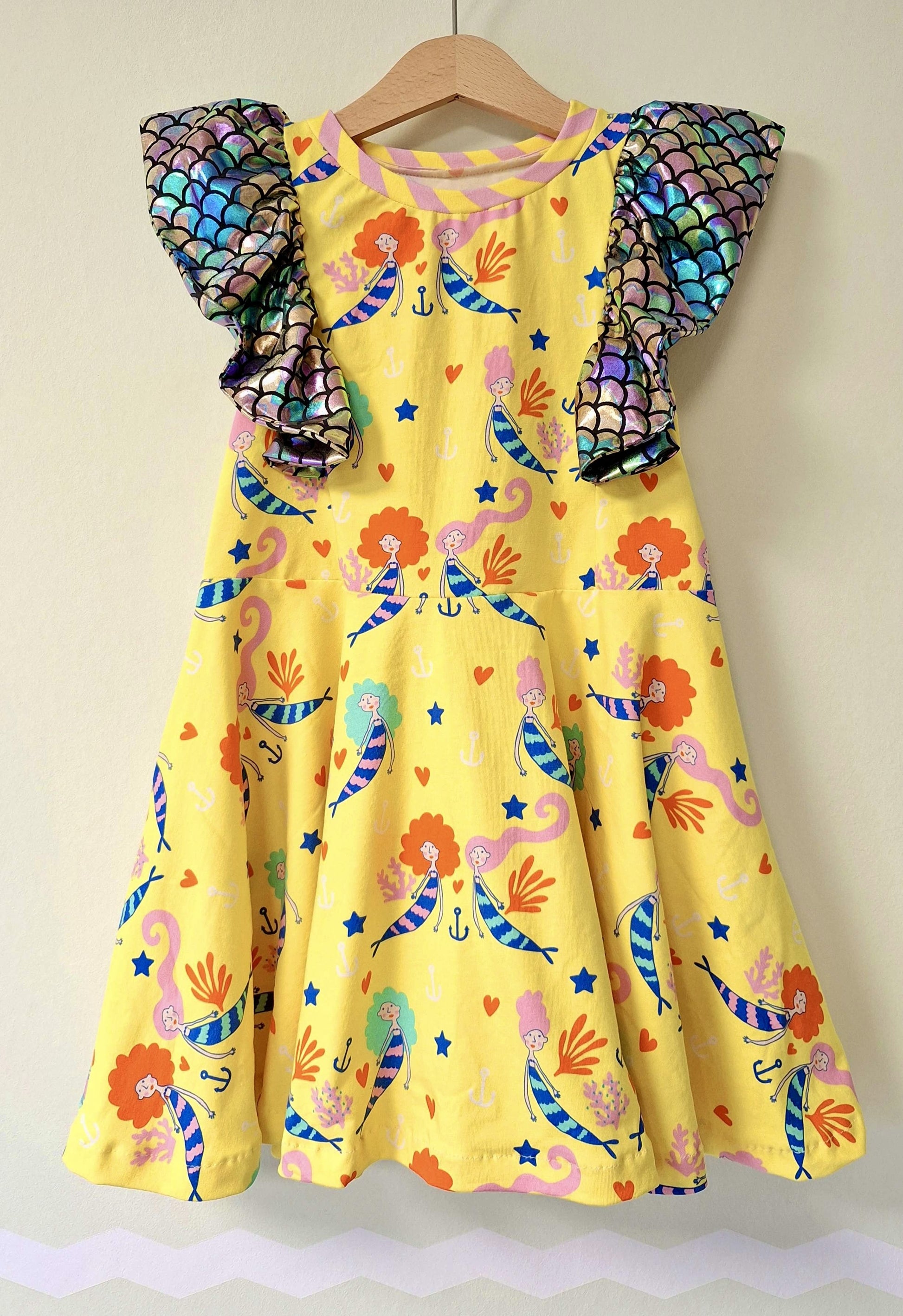 Schnittmuster Kinderkleid Mathilda genäht aus gelbem Jersey mit Meerjungfrauen-Print – große Schulterrüschen aus schimmerndem Schuppen-Stoff, ausgestellter Rock, Gr. 98–146