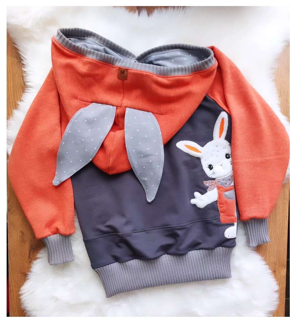 Schnittmuster Hoodie Mika aus orangefarbenem und grauem French Terry – Variante mit langen Hasenohren, Bauchtasche mit Hasen-Applikation, Flatlay auf weißem Fell
