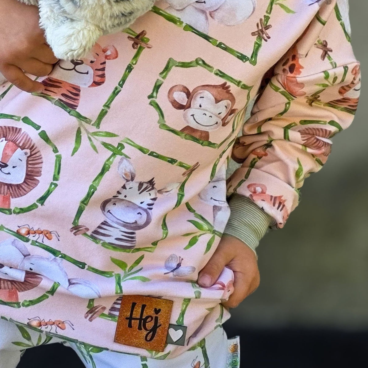 Nahaufnahme eines Hoodies aus Safari-Stoff: Löwe, Affe und Zebra in Bambusrahmen, dazu eine Ameise und ein Schmetterling