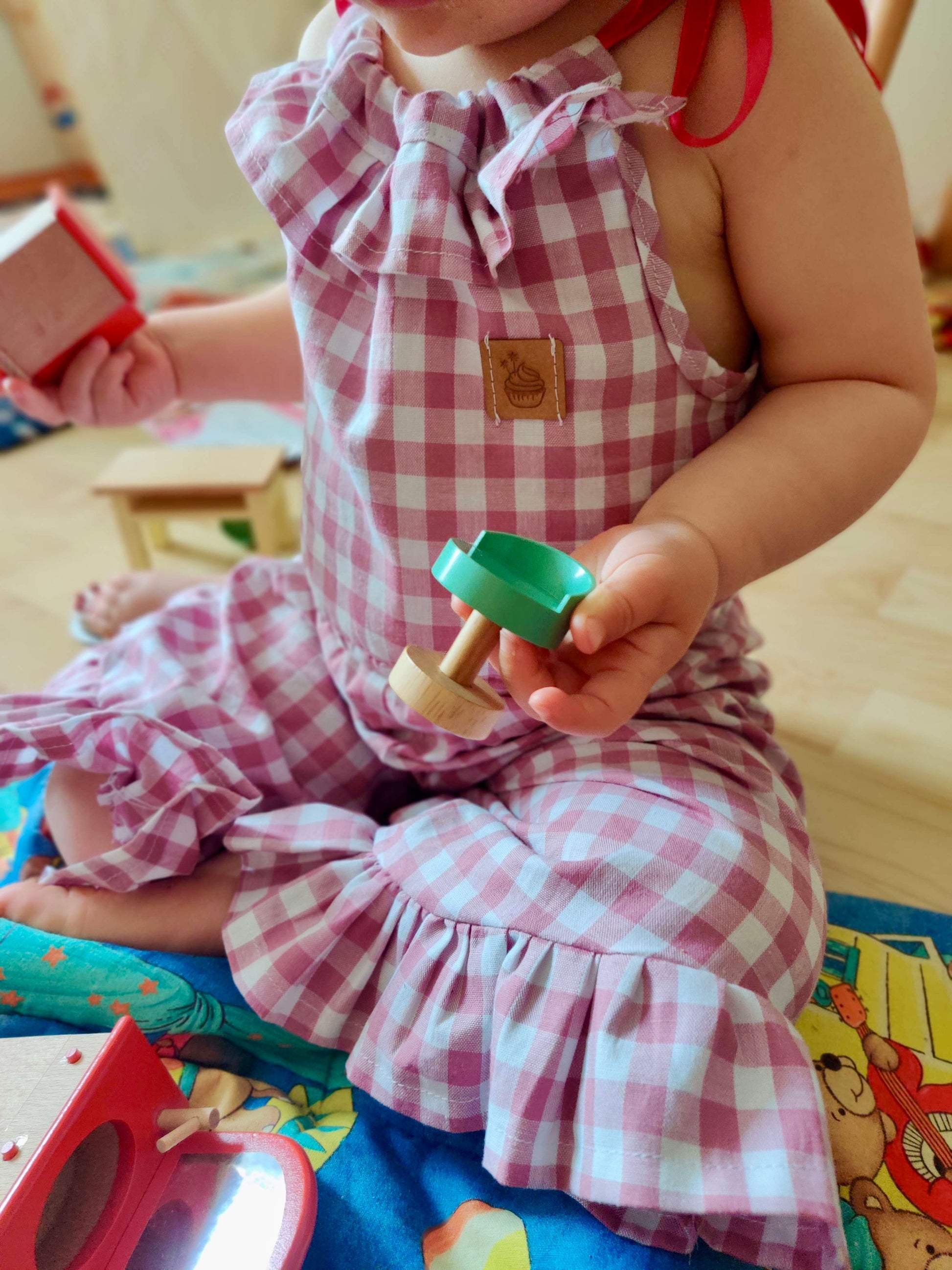 Schnittmuster Jumpsuit Pernille aus rosa Musselin im Vichy-Karo – Kleinkind spielt auf Boden, Variante mit Rüschen am Saum, weiche Hosenbeine, Gr. 92