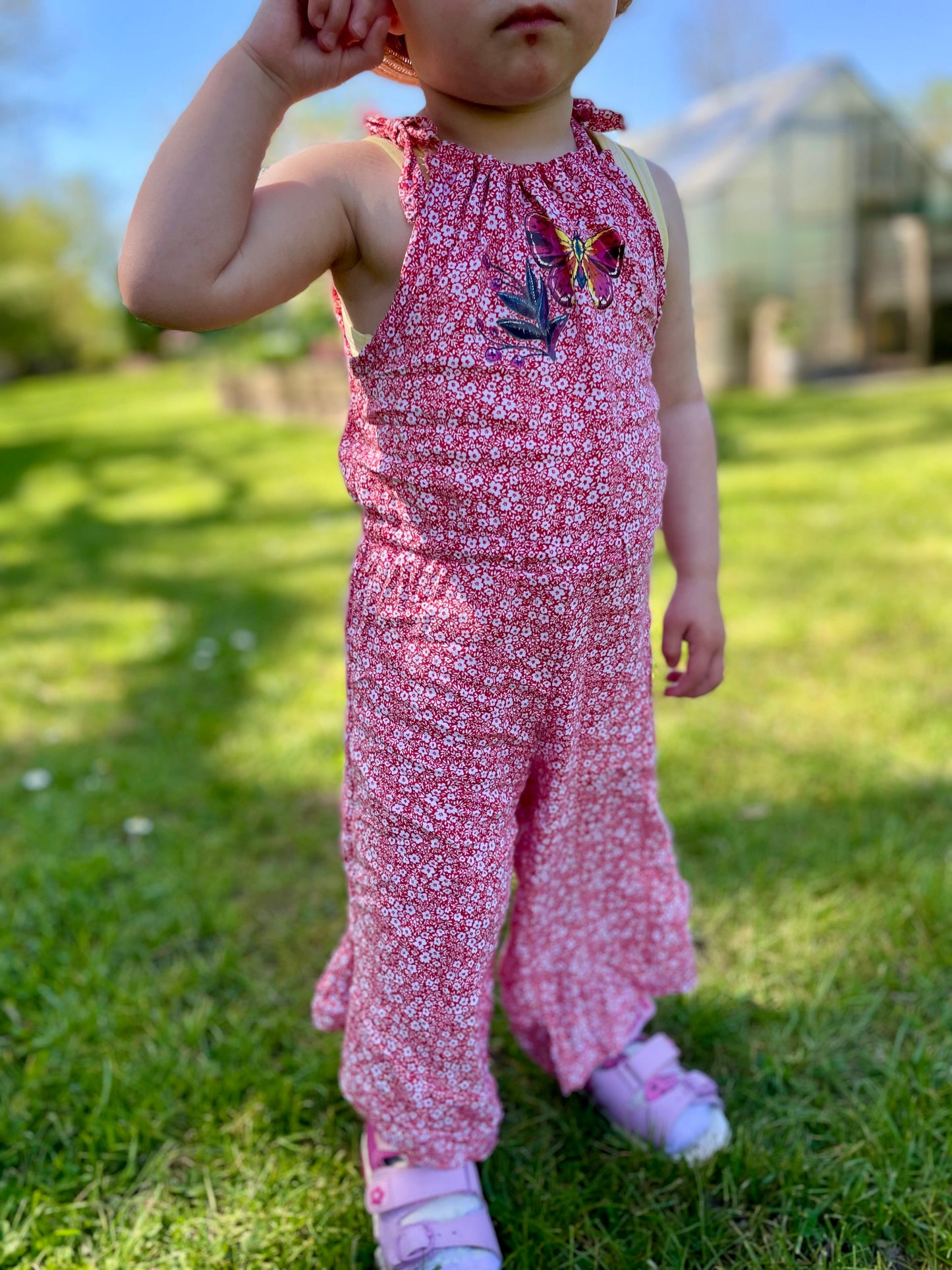 Schnittmuster Jumpsuit Pernille aus rotem Webware-Stoff mit weißem Blumenprint – Kleinkind trägt Jumpsuit auf Wiese, lange Hosenvariante, Gr. 92–98
