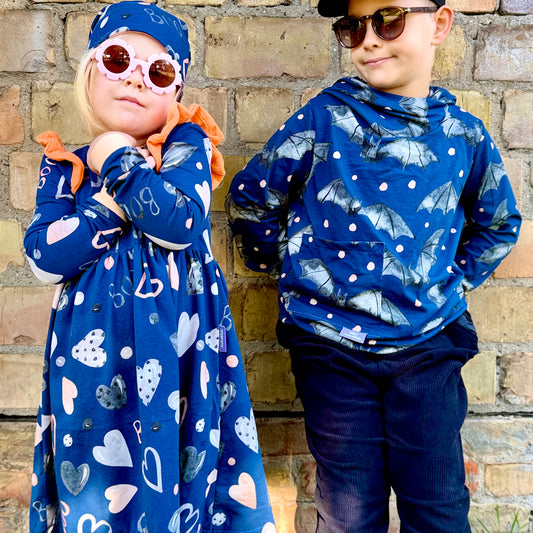 Mädchen im Kleid aus Gespensterbande Stoff mit Herzen und BOO-Schriftzug, orangen Musselin-Rüschen und passender Beanie