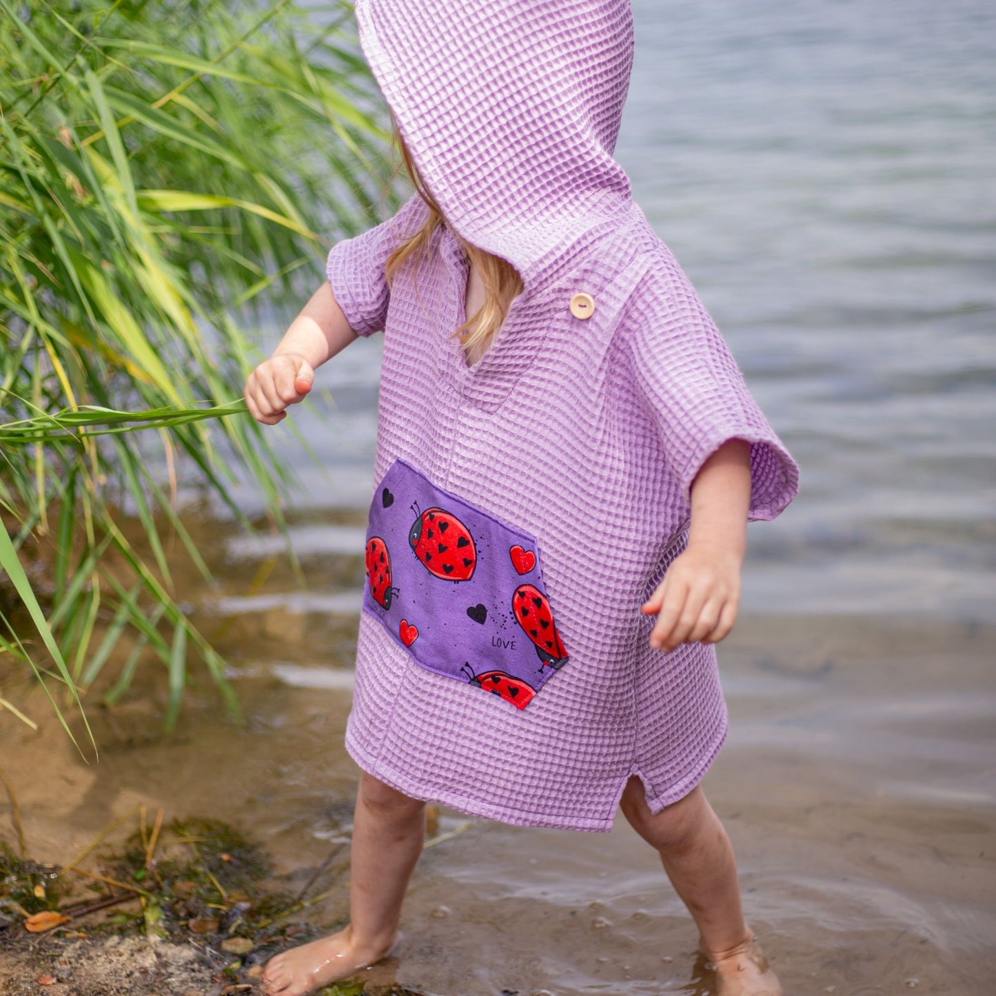 Schnittmuster Poncho Jonte Detailansicht Bauchtasche – lila Waffelpiqué mit Bauchtasche aus Marienkäfer-Kontrastprint, Holzknopf, Seitenschlitz sichtbar