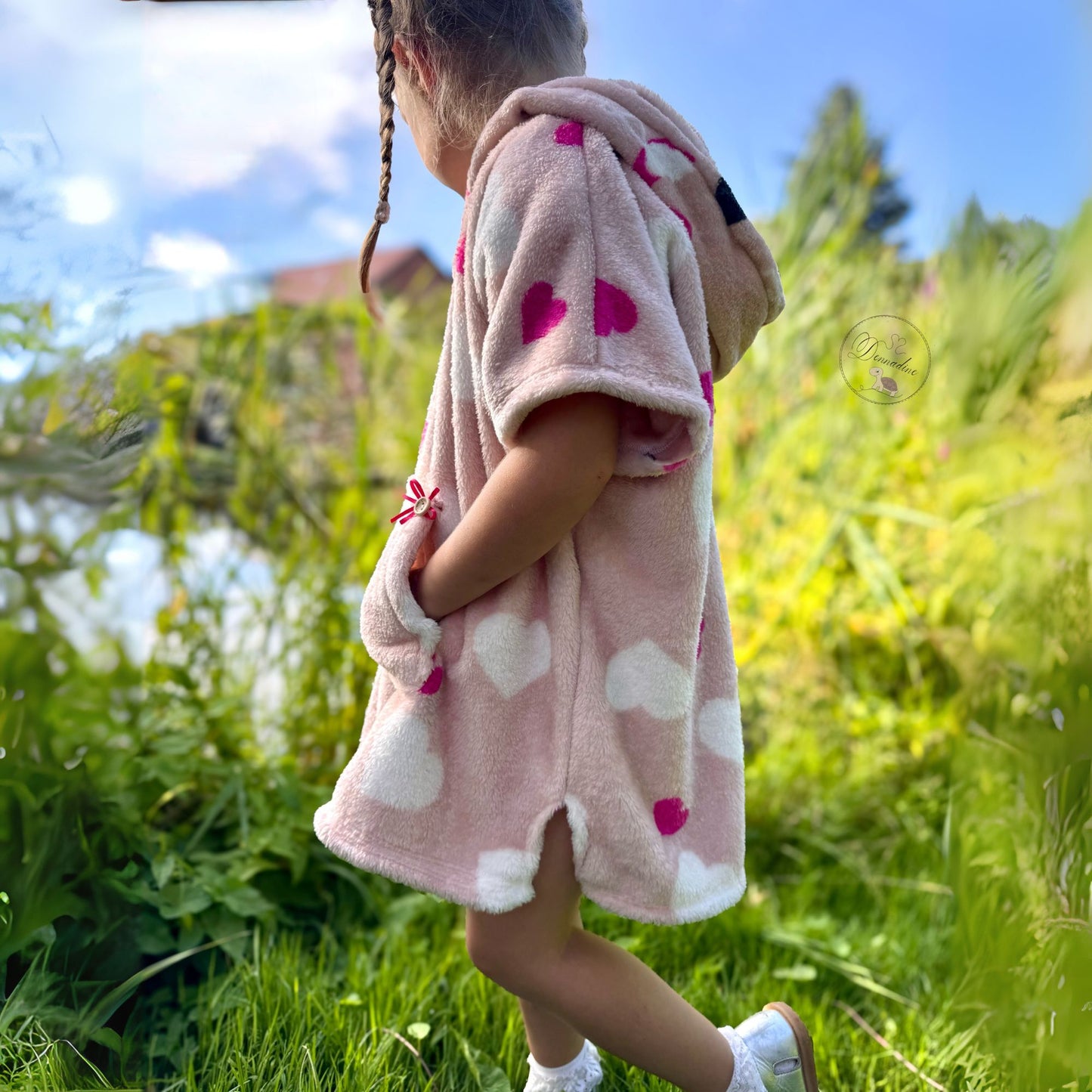 Schnittmuster Poncho Jonte aus rosafarbenem Plüsch mit Herzmuster – Variante mit Kapuze, Bauchtasche mit Holzknopf, Kind läuft auf Sommerwiese