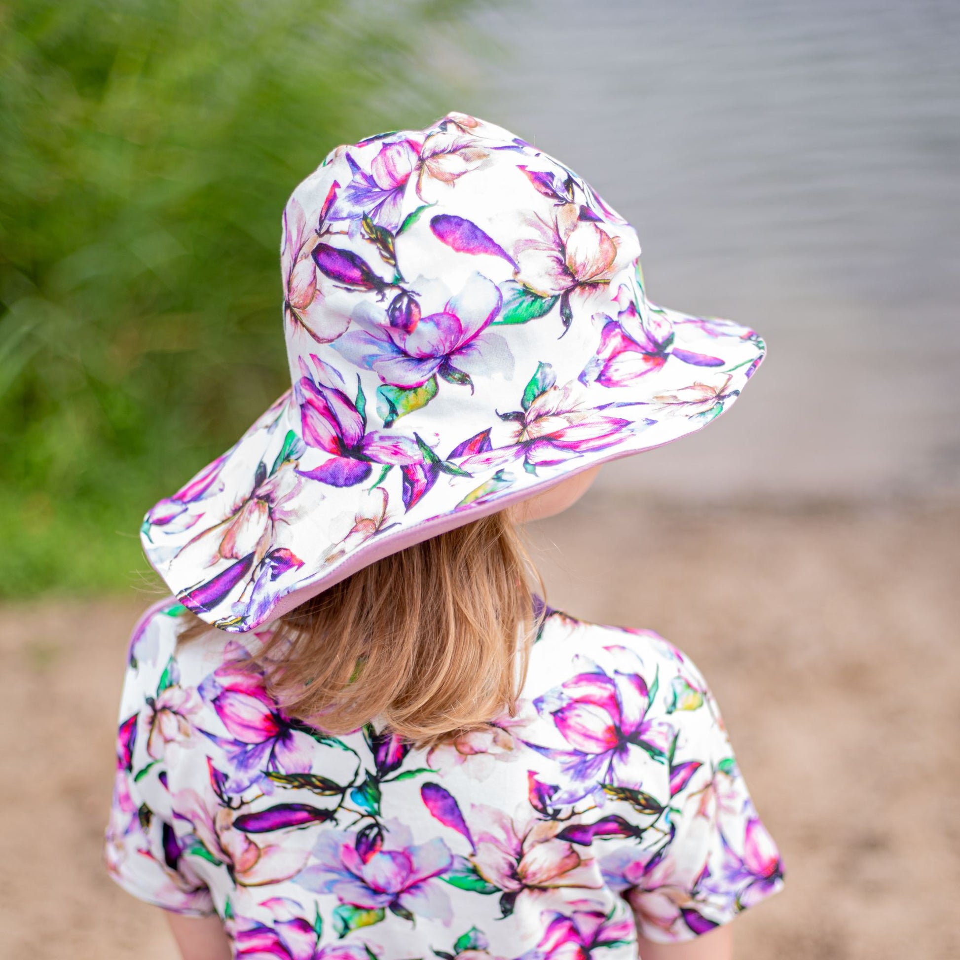 Schnittmuster Sommerhut Salva aus weißem Jersey mit lila-rosa Blumenprint – breite Krempe, Kind trägt selbstgenähten Sonnenhut am Wasser, Größe für Kleinkinder