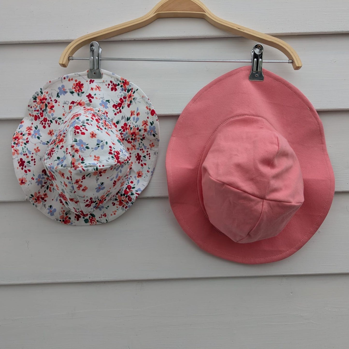 Schnittmuster Sommerhut Salva als Wendehat – links Kindergröße aus weißem Jersey mit rotem Blumenprint, rechts Erwachsenengröße aus rosa Uni-Jersey, Größenvergleich auf Kleiderbügel