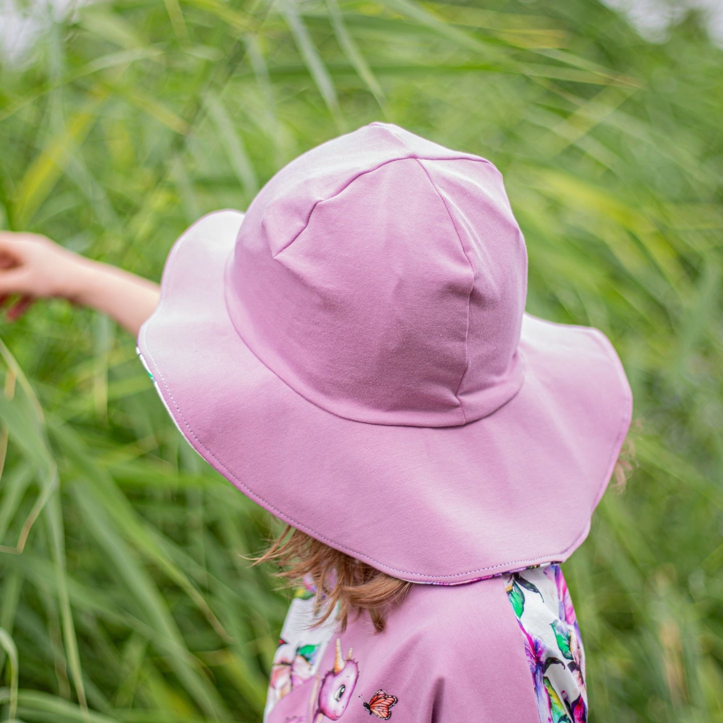 Schnittmuster Sommerhut Salva aus rosafarbenem Jersey – breite Krempe schützt Gesicht und Nacken, Kind trägt selbstgenähten Sommerhut im Grünen, Rückenansicht
